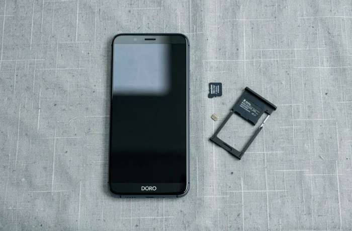 Vue du dessus d'un téléphone Doro avec une carte SD, un outil d'éjection et le tiroir ouvert disposés sur une surface en lin gris clair