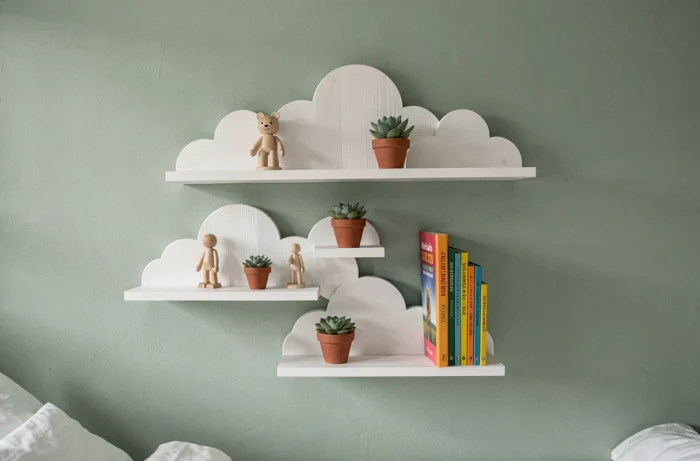 Étagères murales en forme de nuages et de montagnes en bois blanc sur un mur vert sauge dans une chambre d'enfant
