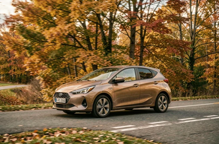 Voiture hybride roulant sur une route de campagne bordée d'arbres aux couleurs automnales